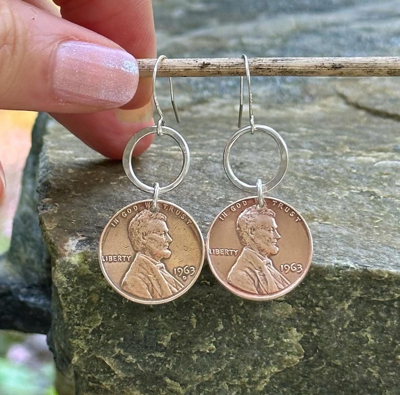 May include: A pair of silver hoop earrings with a 1963 US penny attached to each hoop. The pennies are copper colored and feature the profile of Abraham Lincoln.