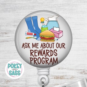 May include: A circular badge reel featuring a cartoon illustration of blue socks, a toothpaste tube, a toothbrush, a gold medal, a water pitcher, a green can, a sandwich, and a tissue box. The text reads: ASK ME ABOUT OUR REWARDS PROGRAM.