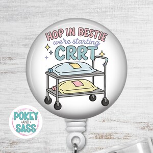 May include: A circular badge reel featuring a medical cart illustration with two fluid bags. The text reads "HOP IN BESTIE we're starting CRRT" in pink, purple, and blue. Small star icons surround the cart, and a small logo reads "POKEY AND SASS".