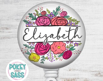 May include: A circular white badge reel featuring a colorful floral illustration of pink, red, and yellow flowers with green leaves. The name Elizabeth is printed in black script across the center between two horizontal black lines.