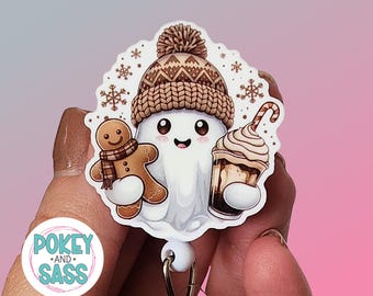 May include: A badge reel featuring a white ghost character wearing a brown knit beanie with a pom-pom. The ghost holds a brown gingerbread cookie and a cup of coffee with a candy cane. Small brown snowflakes surround the ghost on a white background.