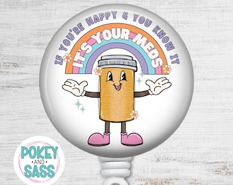 May include: A circular badge reel featuring a cartoon pill bottle with arms and legs, a rainbow, and small flowers. The text reads: IF YOU'RE HAPPY & YOU KNOW IT IT'S YOUR MEDS. The design includes white, orange, pink, and blue colors on a white background.