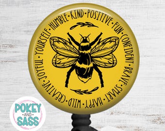 May include: A yellow badge reel with a black and yellow bee illustration. The badge reel has the words "Joyful, Yourself, Humble, Kind, Positive, Fun, Confident, Brave, Smart, Happy, Wild, Creative" around the bee. The badge reel also has the text "Pokey and Sass".