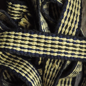 Peut inclure: Gros plan sur un ruban tissé à rayures noires et jaunes. Le ruban est fait d'un matériau doux et texturé et a un léger brillant.