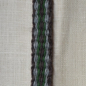 Puede incluir: Primer plano de una correa tejida de tela marrón, verde y gris. La correa está hecha de lana y tiene una superficie texturizada.