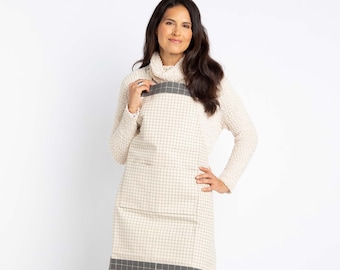 May include: A white and gray checkered apron with a large pocket and a gray trim. The apron is worn by a person with long brown hair.