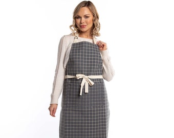 May include: A gray and white checkered apron with a cream-colored fabric tie and two pockets. The apron has adjustable straps.