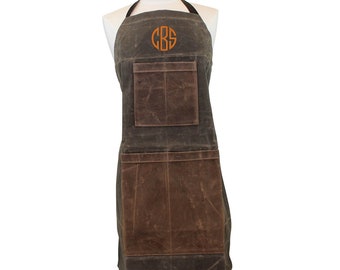 May include: A brown and green canvas apron with a large pocket on the front and two smaller pockets on the sides. The apron has a monogrammed "CBS" in orange on the chest.
