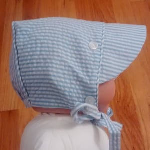May include: A blue and white striped baby bonnet with a brim and a tie at the back.