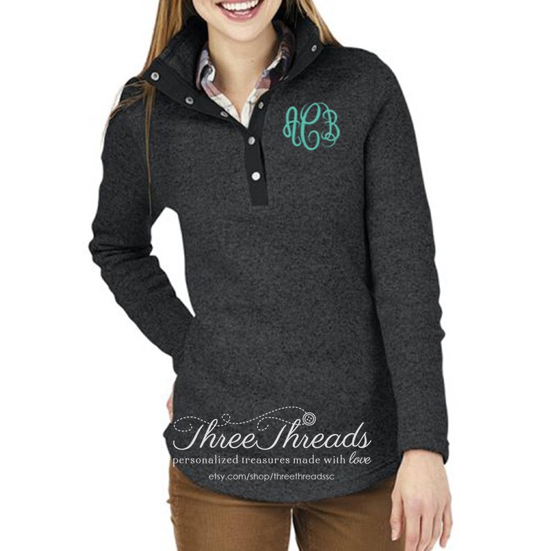 May include: A charcoal gray pullover with a snap button placket and a teal monogram on the chest. The pullover has a mock neck and long sleeves. The text "Three Threads" is printed on the bottom of the pullover.