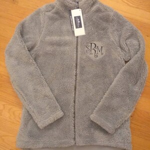 May include: A grey fleece jacket with a zip fastening and a monogrammed "SRM" on the front. The jacket has a soft, fuzzy texture.