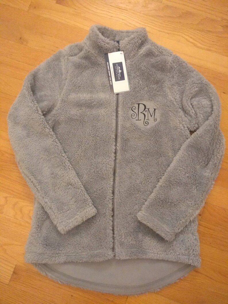 May include: A grey fleece jacket with a zip fastening and a monogrammed "SRM" on the front. The jacket has a soft, fuzzy texture.