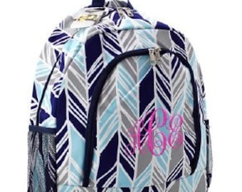 May include: A blue, gray, and white chevron patterned backpack with a pink monogram. The backpack has a zippered front pocket and mesh side pockets.
