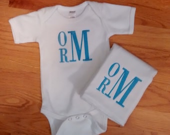 May include: White baby onesie and burp cloth with blue embroidered letters spelling "OMR" on both items.