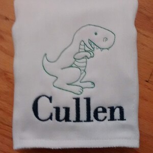 May include: White towel with a green embroidered dinosaur and the name "Cullen" in black embroidery.