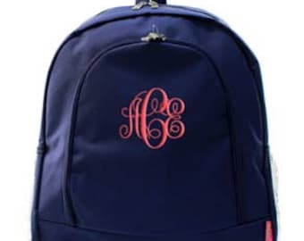 May include: A navy blue backpack with a large pink monogram embroidered on the front.