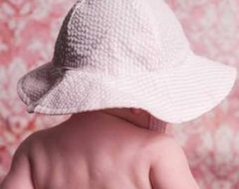 May include: A white sun hat with a pink and white striped pattern. The hat has a wide brim and a chin strap.