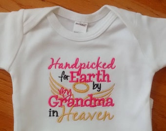 May include: White baby onesie with pink and gold embroidery that reads "Handpicked for Earth by my Grandma in Heaven".