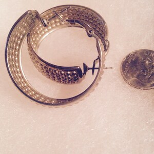 May include: A pair of silver hoop earrings with a textured surface. The earrings are closed with a hinged clasp.