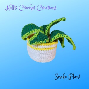 May include: A crocheted snake plant in a white pot with a yellow rim. The plant is green and yellow and has a textured surface. The pot is sitting on a blue background. "Nell's Crochet Creations" and "Snake Plant" are written in the image.