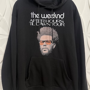 May include: Black hooded sweatshirt with a white graphic print of The Weeknd with the text "the weeknd after hours til dawn tour".