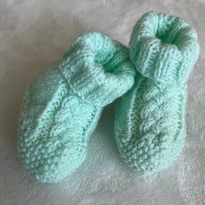 May include: A pair of light green knitted baby booties with a cable knit pattern.
