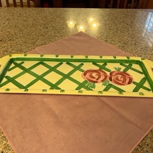 May include: A yellow ceramic serving tray with a green and white checkered pattern and two pink roses painted on the surface.