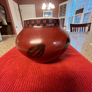 May include: A red ceramic pot with black geometric designs and a black and white checkered band around the top.