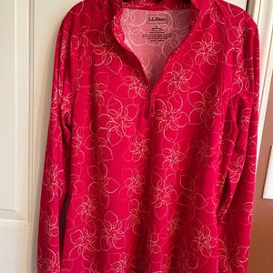 May include: A long-sleeved, red shirt with a floral pattern. The shirt has a zipper up the front and the brand name "L.L.Bean" is visible on the tag.