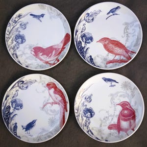 May include: Set of four white ceramic dinner plates with blue and gray floral designs and red and gray birds. Each plate features a different bird.