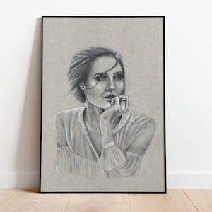 Puede incluir: Retrato a l&aacute;piz enmarcado de una mujer con el pelo corto, apoyando la barbilla en la mano. La obra de arte es en escala de grises, con un fondo claro y un marco negro. La mujer lleva una blusa de color claro.