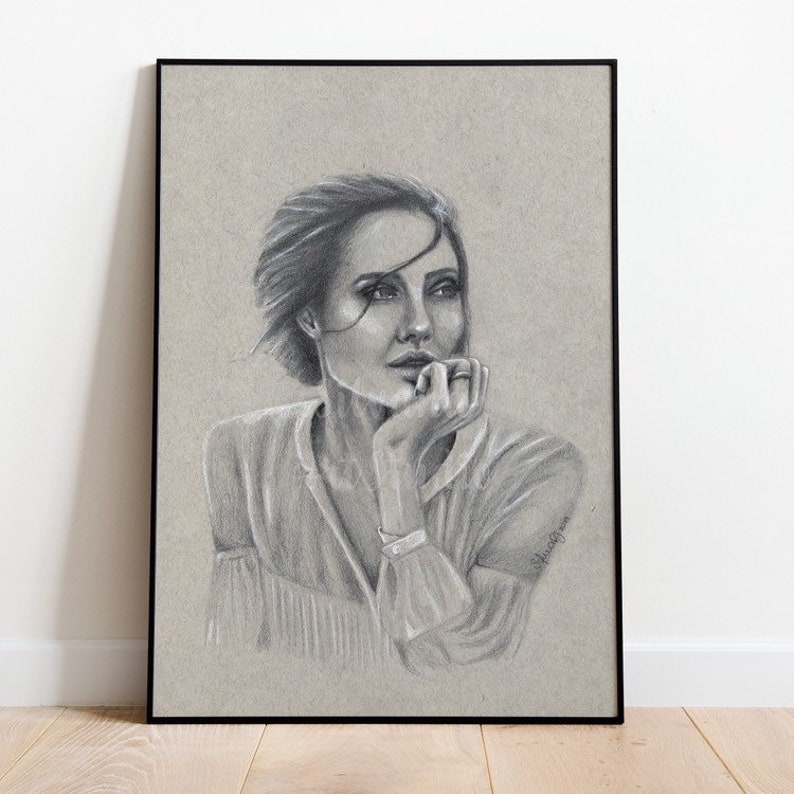 Puede incluir: Retrato a l&aacute;piz enmarcado de una mujer con el pelo corto, apoyando la barbilla en la mano. La obra de arte es en escala de grises, con un fondo claro y un marco negro. La mujer lleva una blusa de color claro.