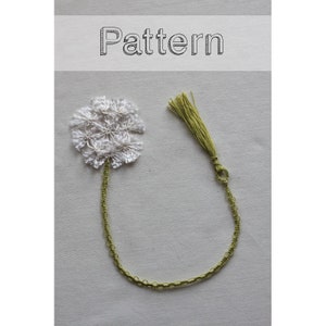 May include: A white crocheted flower with a green stem and tassel attached to a green crocheted chain. The chain is looped to form a bookmark. The image has the word "Pattern" written above the bookmark.