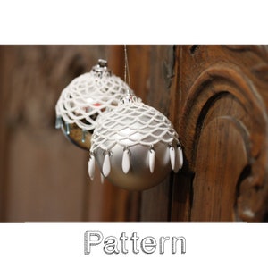 May include: Two silver Christmas ornaments with white beaded netting and dangling teardrop accents. The ornaments hang in front of a wooden background. The word "Pattern" is at the bottom of the image.