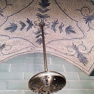 Könnte beinhalten: Ein Duschkopf mit einem runden, silberfarbenen Duschkopf und einem langen, silberfarbenen Arm. Der Duschkopf ist an einer Decke mit einem Mosaikmuster montiert.