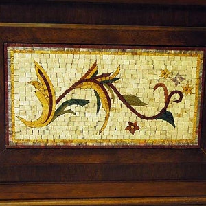 Könnte beinhalten: Ein dekorativer Holzrahmen mit einer Mosaik-Einlage aus Fliesen, die ein stilisiertes Blumenmuster in Gelb-, Rot-, Grün- und Brauntönen zeigt.