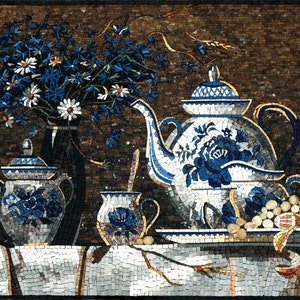 Può includere: Un'opera d'arte a mosaico di natura morta con una teiera blu e bianca, una zuccheriera, un creamer e un bouquet di fiori blu e bianchi in un vaso nero. L'opera d'arte è su una tovaglia bianca con uno sfondo marrone.