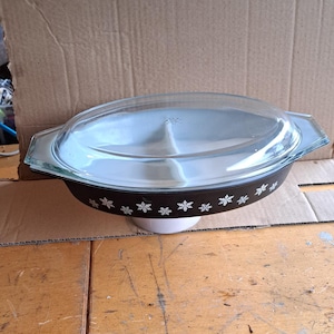 Puede incluir: Una fuente para hornear dividida en blanco y negro con tapa de vidrio. La fuente está decorada con un patrón de copos de nieve.