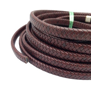 May include: A close-up of a brown leather cord, braided in a basket weave pattern. The cord is coiled and ready for use in crafting projects.