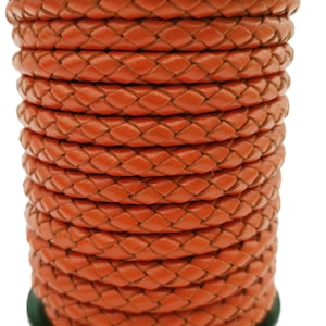 May include: A close-up of a spool of orange braided leather cord. The cord is tightly wound and has a smooth, polished finish.