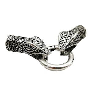 May include: Silver-toned metal clasp with two snake head designs. The clasp is designed to be used as a connector for a necklace or bracelet.
