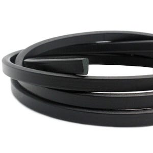 May include: Black leather cord, approximately 5mm wide, coiled on a white background.