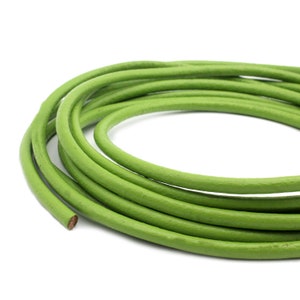 Op de afbeelding: Opgerolde groene leren koord tegen een witte achtergrond. Het koord is een levendige groene kleur, met een gladde, afgeronde textuur. Het afgesneden uiteinde toont een bruin binnenwerk. Geschikt voor het maken van sieraden en knutselwerk.