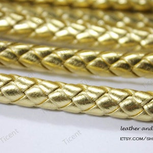 May include: Gold braided leather cord. The cord is woven in a diamond pattern and has a shiny, metallic finish.