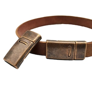 May include: Two antique brass magnetic clasps for leather bracelets or necklaces. The clasps are rectangular and have a slightly textured finish.