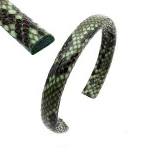 May include: A green and brown snakeskin leather headband. The headband is made of a single piece of leather that is curved into a circle.