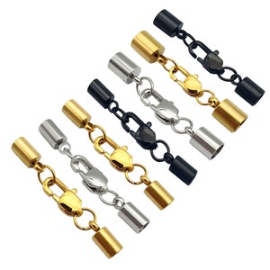 Op de afbeelding: Set van zes gouden, zilveren en zwarte metalen eindkappen met karabijnhaken. De eindkappen zijn cilindrisch en hebben een gladde afwerking. De karabijnhaken zijn zilverkleurig.