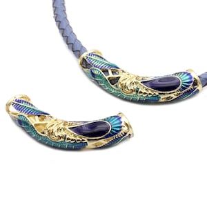 May include: Two gold-toned metal cord ends with blue and green enamel detailing. The ends are shaped like a curved horn with a decorative design.
