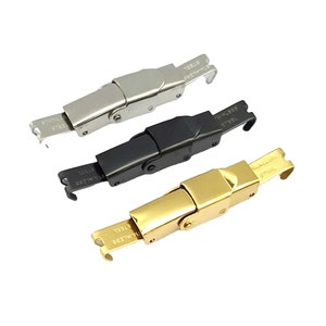 May include: Three stainless steel watch clasps in silver, black, and gold. Each clasp has a rectangular body with a hinged section and a hook closure. The words "STAINLESS STEEL" are printed on the hook end of each clasp.
