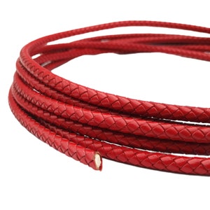 May include: Red braided leather cord, a close-up of the braided texture. The cord is coiled in a circle.